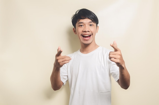 Homme asiatique portant un t-shirt blanc heureux tout en pointant sa main vers l'arrière-plan isolé