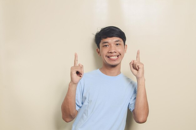 Homme asiatique portant un t-shirt bleu pointant vers le haut fond isolé