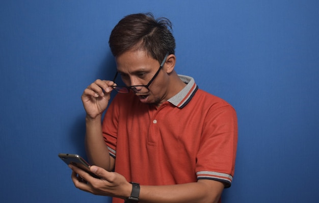 Homme asiatique portant un t-shirt décontracté orange surprenant par les bonnes nouvelles qu'il a reçues de son smartphone