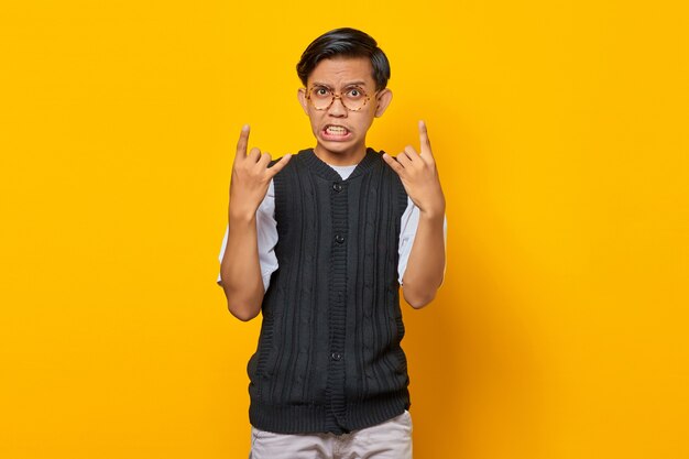 Homme asiatique portant des vêtements décontractés criant avec une expression folle faisant le symbole du rock avec les mains en l'air