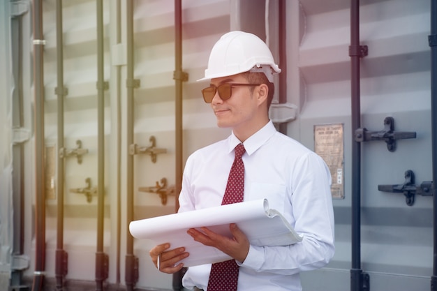 Un homme asiatique porte une chemise blanche et une cravate rouge et un chapeau de sécurité blanc travaille sur un chantier de construction.