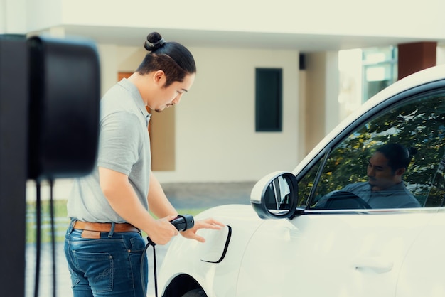 Un homme asiatique progressiste recharge sa voiture EV à la station de charge à domicile