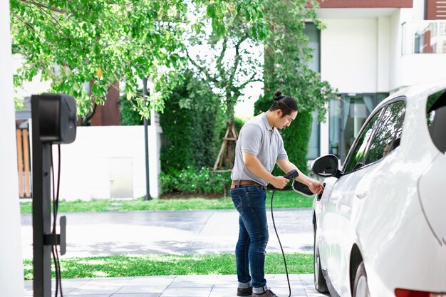 Un homme asiatique progressiste recharge sa voiture EV à la station de charge à domicile