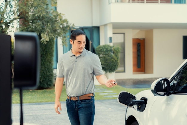 Un homme asiatique progressiste recharge sa voiture EV à la station de charge à domicile