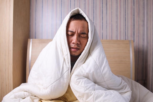 Homme asiatique recouvert d'une couverture chaude sur le lit à la maison attraper froid