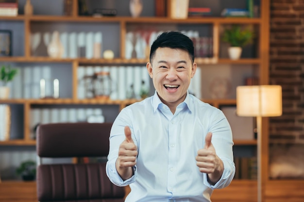 Homme asiatique réussi en chemise travaillant tard dans un bureau classique portrait d'un homme d'affaires heureux regardant la caméra et montrant les pouces vers le haut