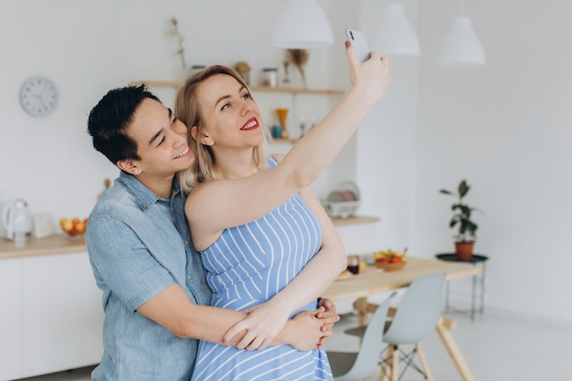 Homme asiatique et sa femme blonde caucasienne passent du temps ensemble et se selfie dans la cuisine