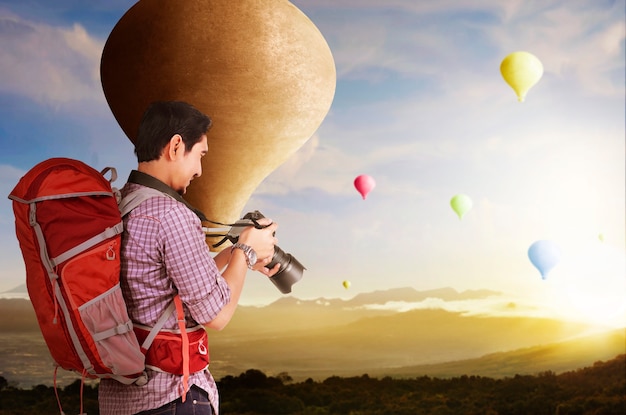 Homme asiatique avec sac à dos et appareil photo regardant un ballon à air coloré volant avec fond de ciel coucher de soleil