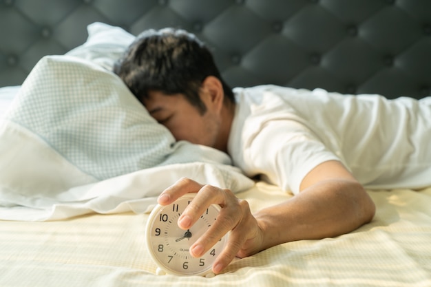 Homme asiatique se réveille le matin et atteint le réveil à la main