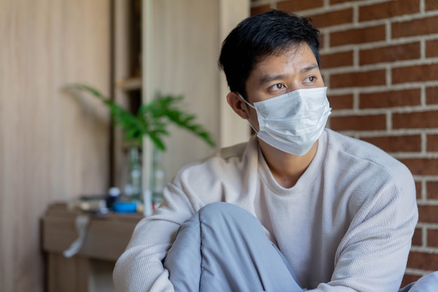 Homme asiatique se réveiller et porter un masque facial dans la chambre le matin pour le temps de quarantaine