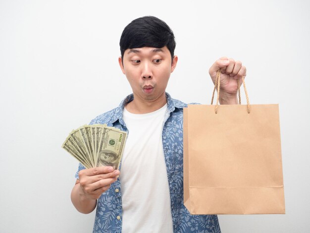 Un homme asiatique se sent excité en tenant beaucoup d'argent en regardant un sac à provisions à la main