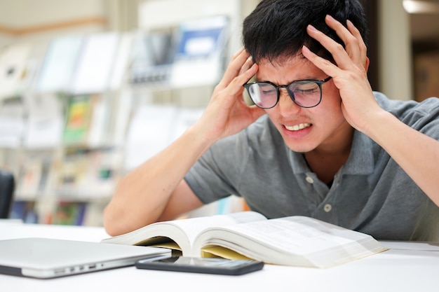 homme asiatique se sentir sérieux après avoir lu des livres pour test à la bibliothèque