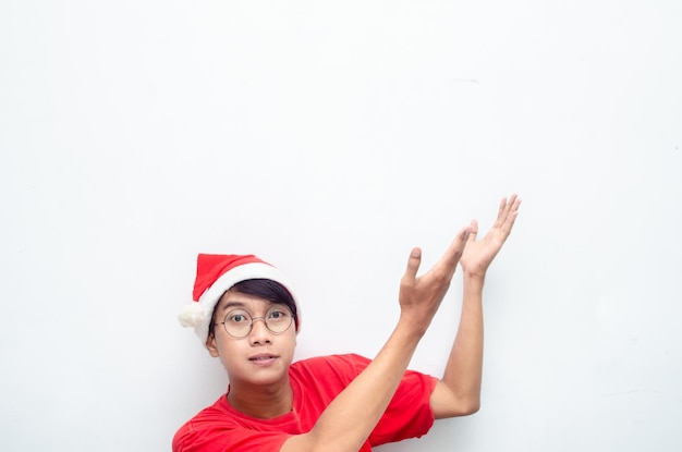 homme asiatique séduisant en vêtements rouges sur le thème de Noël pointant du doigt et présentant quelque chose de marchandises