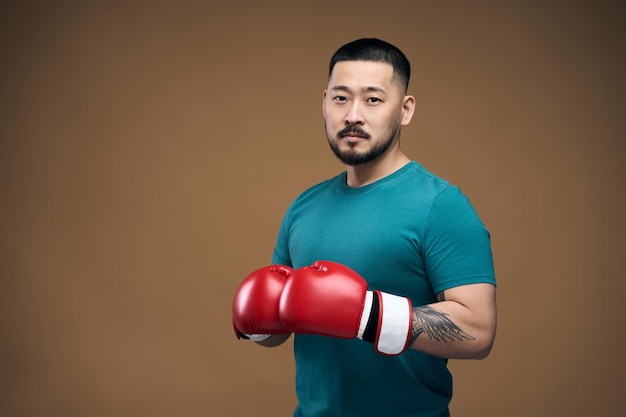 Homme asiatique sérieux en t-shirt portant des gants de boxe rouges debout dans la pose de combat