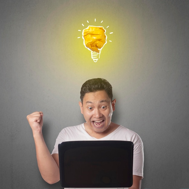 Un homme asiatique souriant heureux avec une ampoule lumineuse faite de papier symbole d'idée et d'innovation