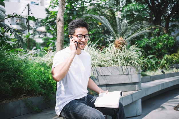 Homme asiatique souriant lisant un livre et parlant sur un smartphone