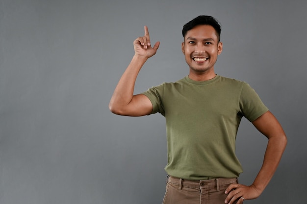 Homme asiatique souriant pointant son doigt vers le haut en se tenant debout sur un fond gris isolé