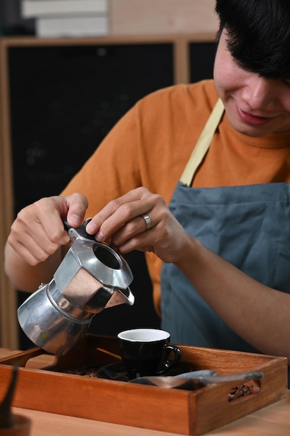 Homme asiatique souriant versant du café de la cafetière moka à une petite tasse de café