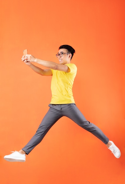 Homme asiatique en t-shirt jaune sautant sur un mur orange