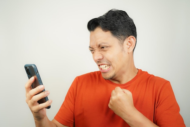 Un homme asiatique en T-shirt orange a l'air excité ou Spirit regarde un message sur son smartphone isolé