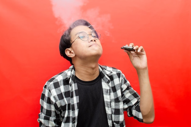 homme asiatique tenant un appareil de vape et entouré d'un nuage de fumée. concept de vapotage et de tabagisme.