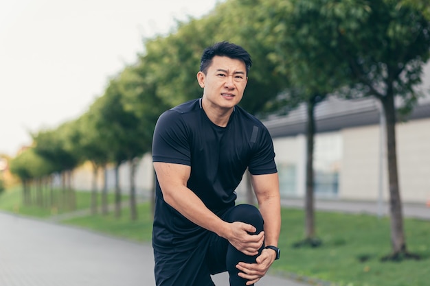 Homme asiatique tenant une douleur au genou après la course et la remise en forme, douleur intense à la jambe