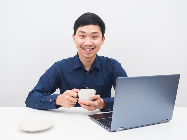 Homme asiatique tenant une tasse de café avec un sourire heureux sur son ordinateur portable au travail sur la table