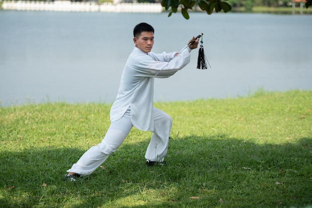 Homme asiatique travaillant avec une épée de Tai Chi le matin au parc, arts martiaux chinois, concept de soins de santé pour la vie.