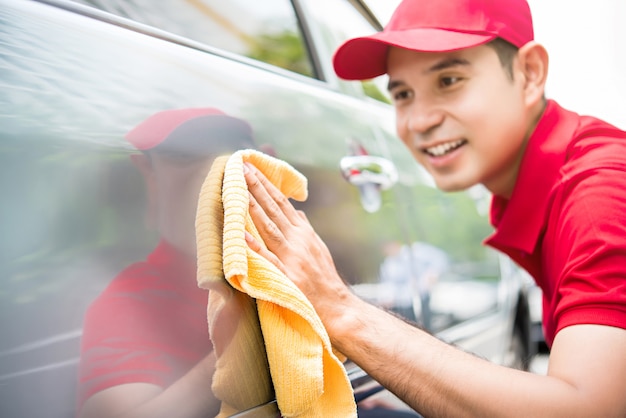 Homme asiatique en uniforme rouge nettoyant une voiture avec un chiffon en microfibre jaune