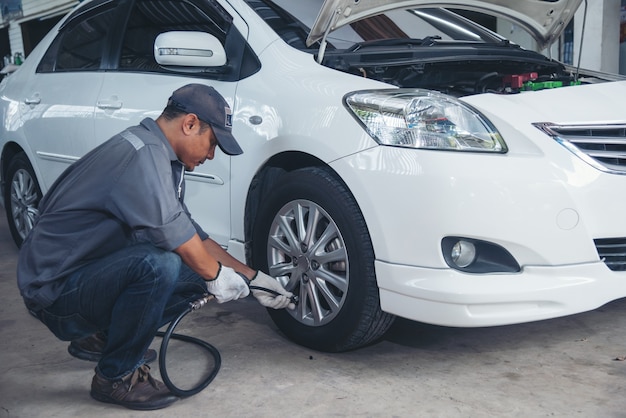 L'homme asiatique vérifie le pneu de la voiture pour le service d'entretien automobile. mécanicien automobile Gonflez le pneu au garage.