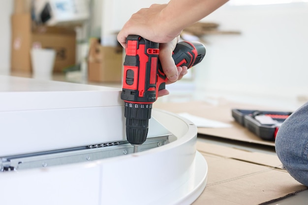 Homme assemblant des meubles de table blancs à la maison à l'aide d'un tournevis sans fil