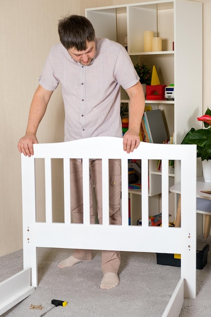 Un homme assemble un lit blanc pour enfant pour un enfant une photo verticale d'un assemblage de meubles