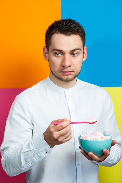 Un homme avec une assiette de guimauves et une cuillère rose. Le gars avec un sourire