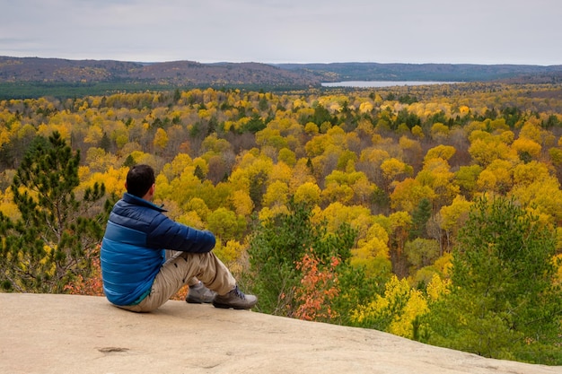Photo un homme assis au bord d'une falaise regardant le paysage d'automne canadien