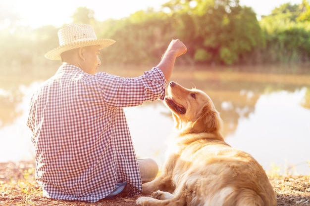 Photo homme assis au bord de la rivière avec un golden retriever brun intelligent au matin