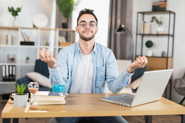 Photo homme assis au bureau avec ordinateur portable et méditant à la maison