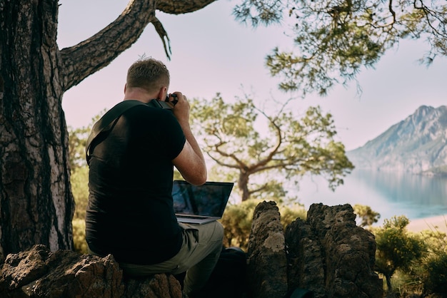 Homme assis au sommet d'une montagne et prenant une photo directement sur un ordinateur portable Travailleur à distance