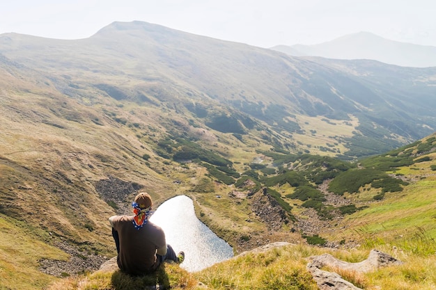 Homme assis au sommet d'une montagne et regardant un lac dans les montagnes