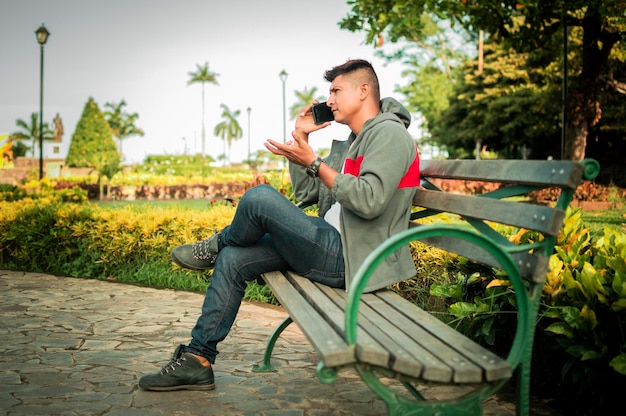 Homme assis sur un banc appelant au téléphone jeune homme assis sur un banc avec un téléphone portable