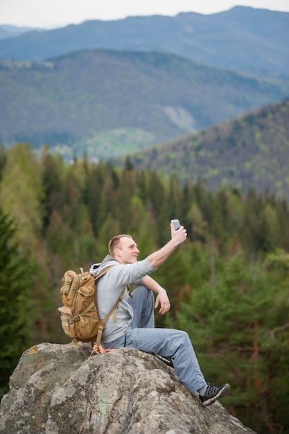 Homme assis sur le bord d'un rocher et fait selfie sur son téléphone