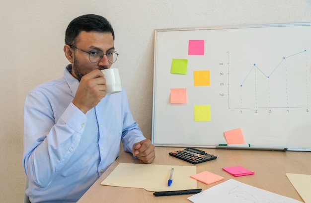 Un homme assis à un bureau buvant d'une tasse blanche