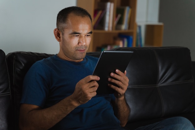 Homme assis sur un canapé, à l'aide d'une tablette PC pour travailler ou se détendre à la maison. travail à domicile concept.