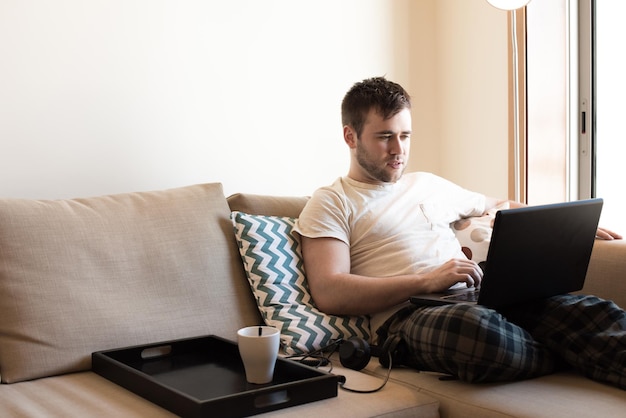 Homme assis sur un canapé avec un ordinateur portable et une tasse de café