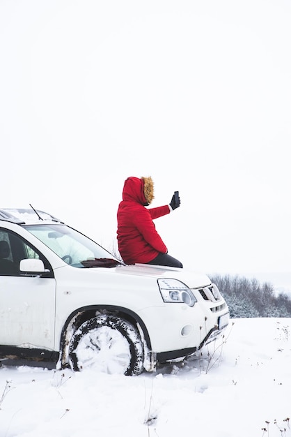 Homme assis sur le capot de la voiture et prise de vue d'une belle vue d'hiver sur son téléphone