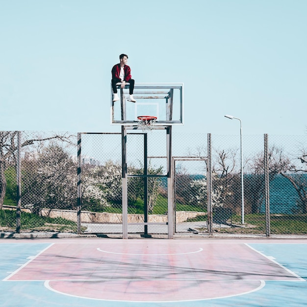Un homme assis sur un cerceau de basket contre le ciel