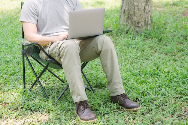 Homme Assis Sur Une Chaise De Camping Et Travaillant Avec Un Ordinateur Portable Dans Le Jardin