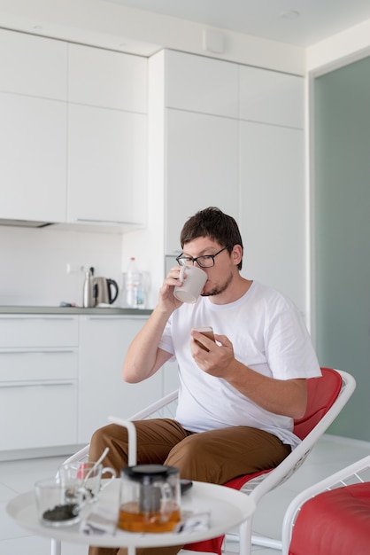 Homme assis sur une chaise devant la télévision tenant une tasse de thé et un téléphone