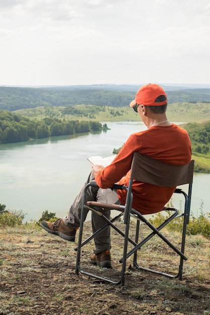 Homme assis dans une chaise de camping à l'extérieur et livre de lecture