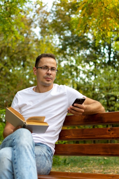 Un homme assis dans un parc avec un téléphone et un livre à lire.