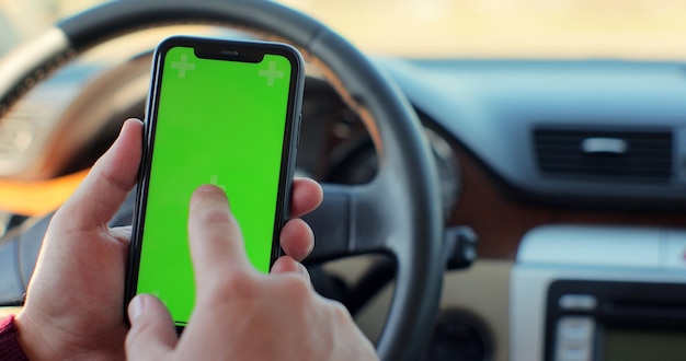 Homme assis dans une voiture moderne utilisant un smartphone avec écran vert chroma key surfant sur Internet et appuyant sur l'écran central.